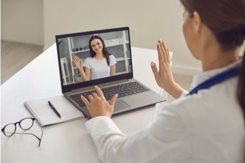 Woman patient greeting her doctor online from laptop screen during videocall